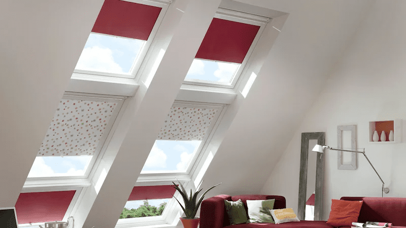 Plissees an Dachschrägenfenstern Dachschrägenfenster mit roten und gemusterten Plissees neben Wohnzimmerbereich